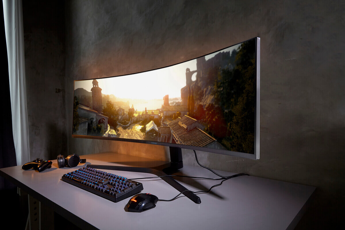 Изогнутый ультраширокий монитор на столе с RGB-клавиатурой и игровой мышью, на экране кадр игры или пейзажа